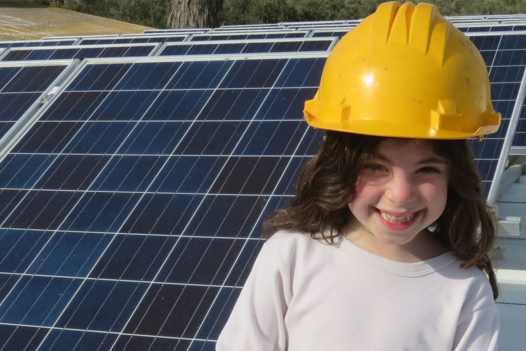 A young girl with a yellow hard hat standing in front of a solar panel