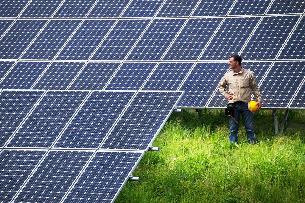 A man with a yellow hard hat standing betwen solar panels