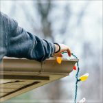 A person placing festive lights on the roof