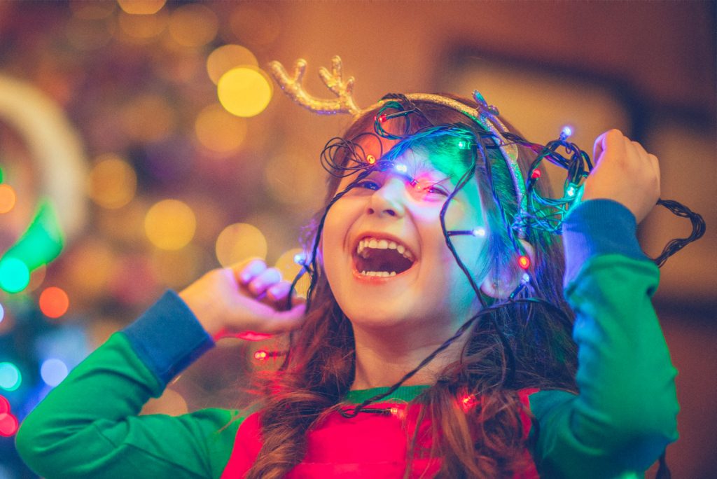 A young girl smiling while playing with Christmas lights
