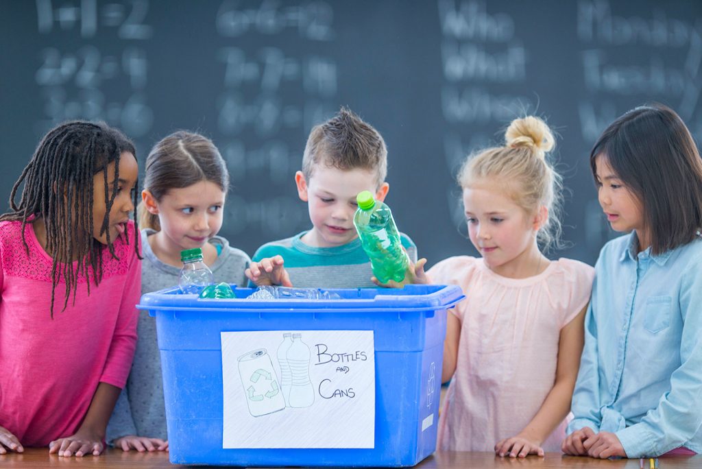 Five children placing plastic bottles in a blue recycling box