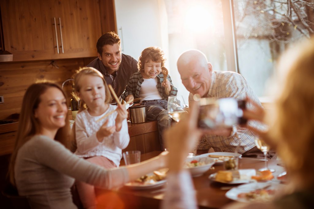 A grandma taking a picture of her smiling family eating dinner