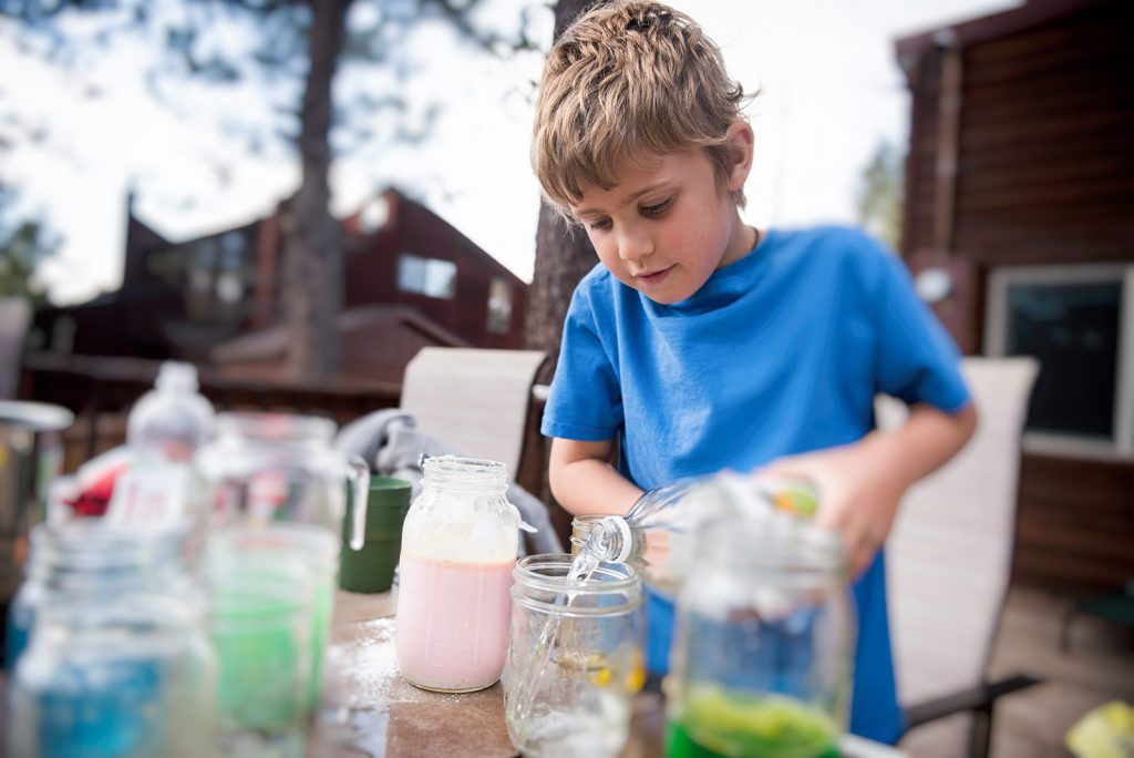 A young boy pouring water into a mason jar
