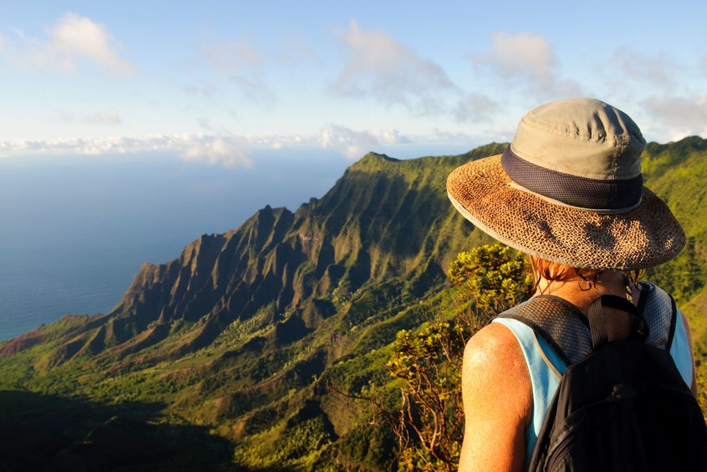 A person with a hat looking at the ocean from atop a green mountain