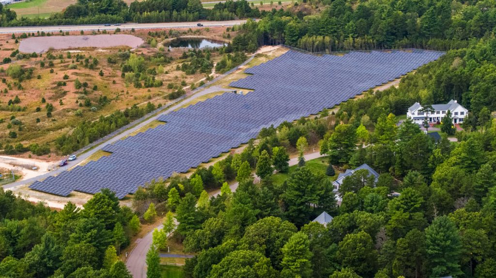 Community solar farm next to trees and a house in Massachusetts