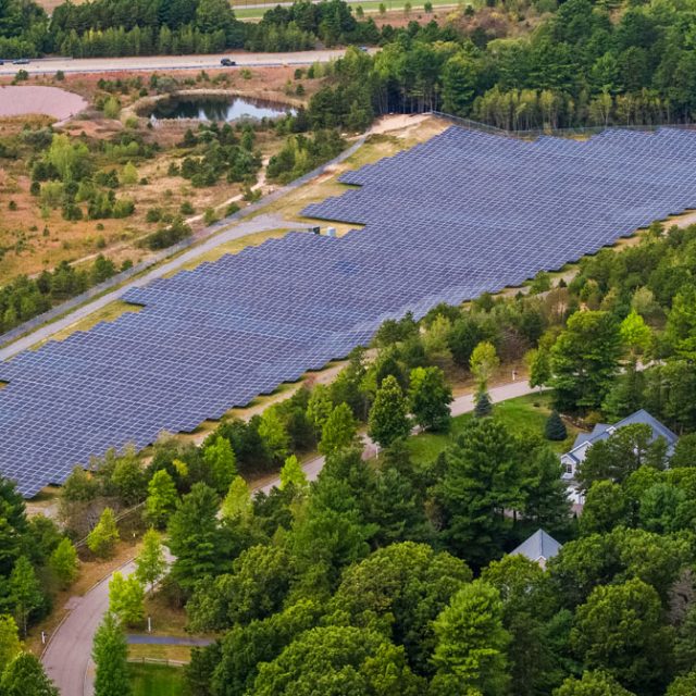 Community solar farm next to trees and a house in Massachusetts
