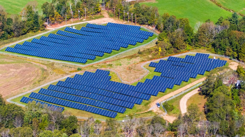 Two community solar farms with blue solar panels surrounded by trees