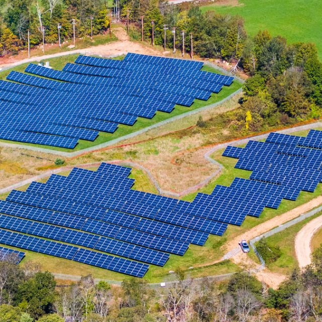 Two community solar farms with blue solar panels surrounded by trees