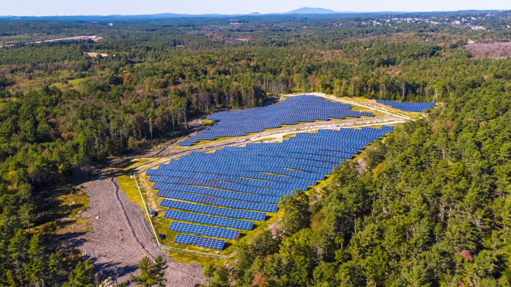 Community solar farms with blue solar panels surrounded by trees