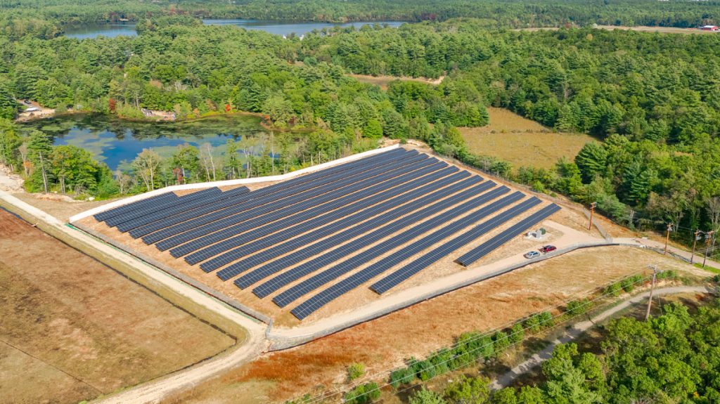 A community solar field next to a dirt road and body of water