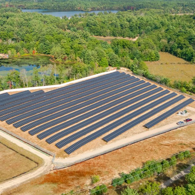 A community solar field next to a dirt road and body of water