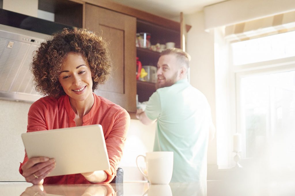 A woman in her kitchen looking at her utility bill on her tablet