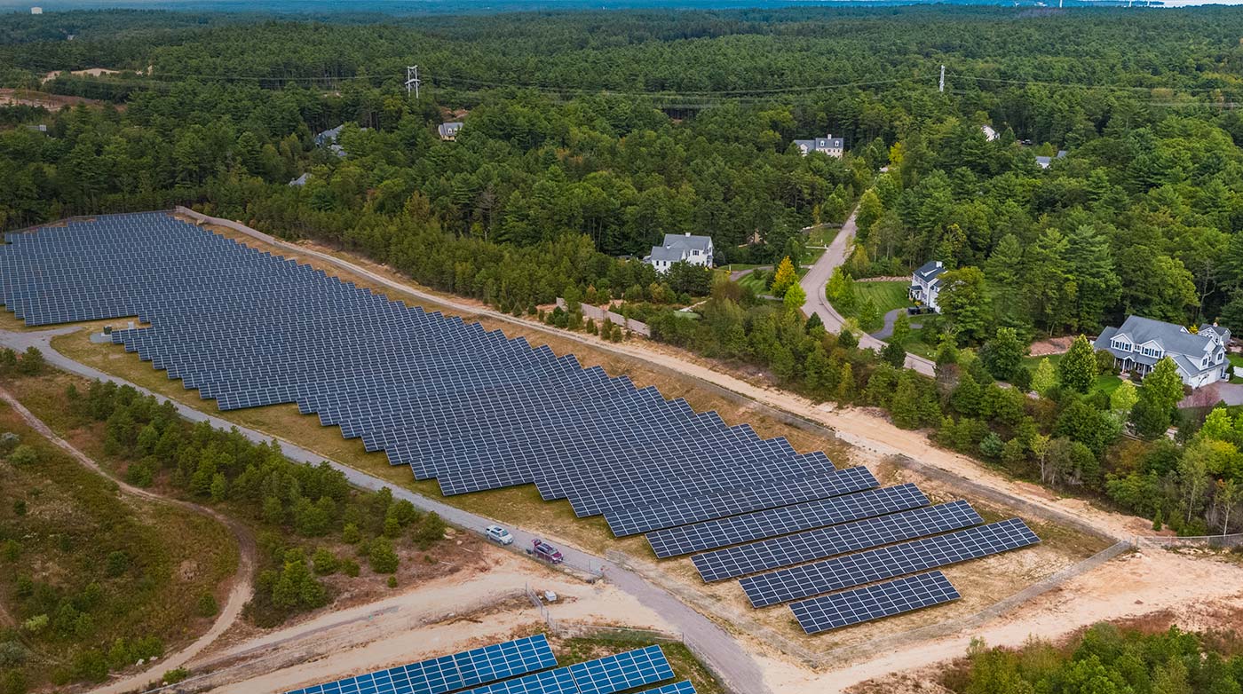 A solar farm next to a wooded area and several houses