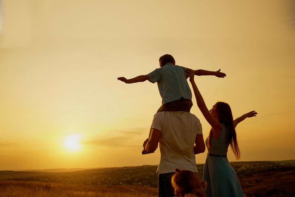 A parent giving a child a ride on their shoulders at sunset