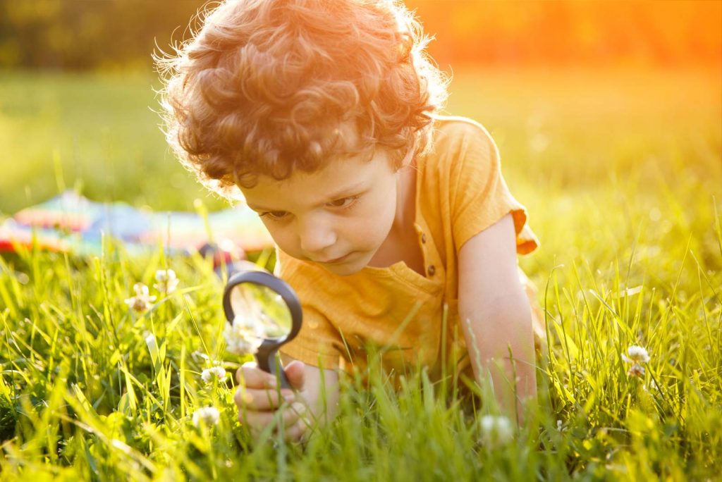 Child looking at the grass with a magnifying glass