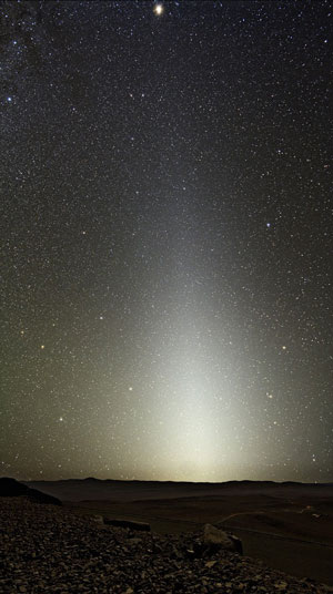 Zodiacal light that extends up the horizon of a black and starry night sky.