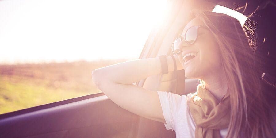young woman laughing by a car window with sun flare
