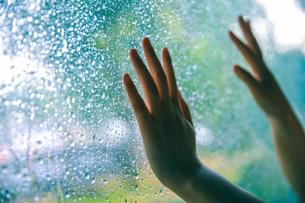 child's hands touching a window with water droplets