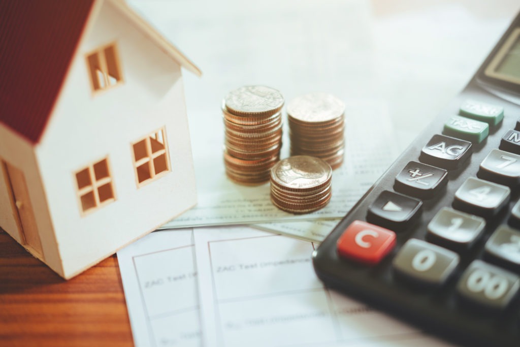 Closeup of a stack of pennies next to a calculator and a model home