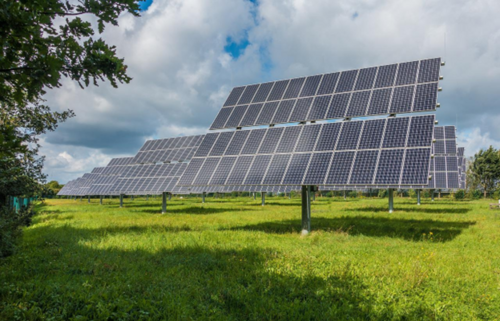 Solar panels from a solar farm sitting in a field on a sunny day. Photo by Mrganso, Pixabay