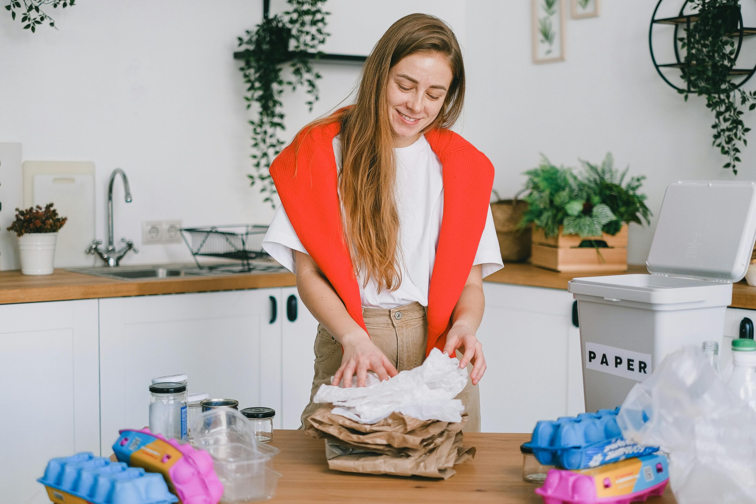 Woman in a minimalist kitchen smiling while organizing a stack of reusable household goods.